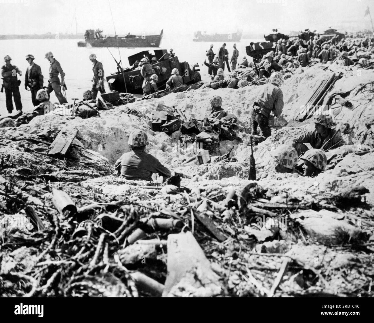 Marshallinseln: 14. Februar 1944, USA Marines nutzen den Schutz durch Muschellöcher am Strand, da andere Ausrüstung aus ihren Landungsbooten auf der Insel ROI-Namur entladen wird. Stockfoto