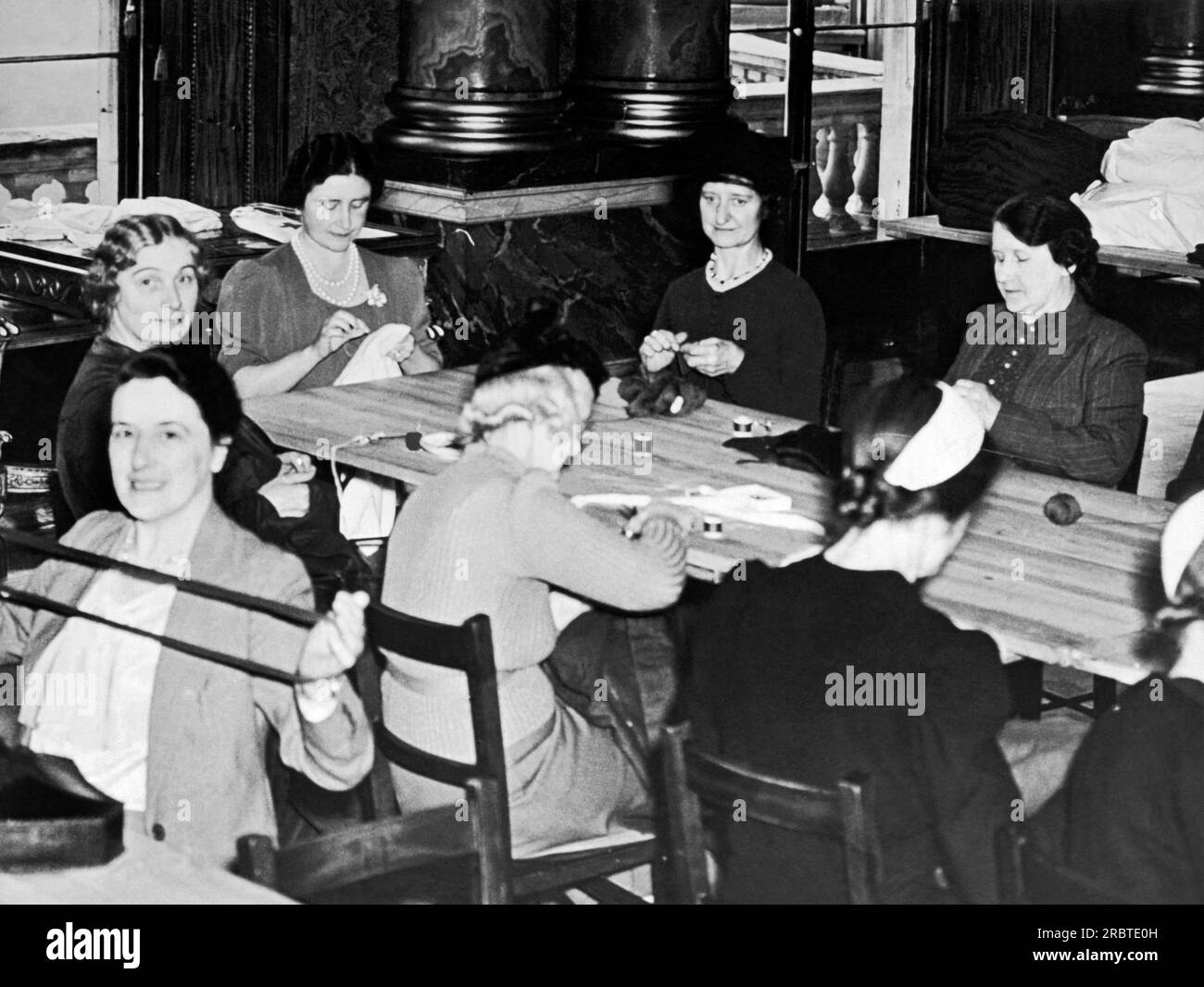 London, England: 21. Oktober 1939 Königin Elizabeth die Königinmutter und ihre Arbeitsgruppe aus Mitarbeitern und Ehefrauen der Mitarbeiter der Royal Mews treffen sich zweimal pro Woche im Blauen Zeichenraum des Buckingham Palace, um Kleidung und Operationsanzüge für das Rote Kreuz herzustellen. Stockfoto
