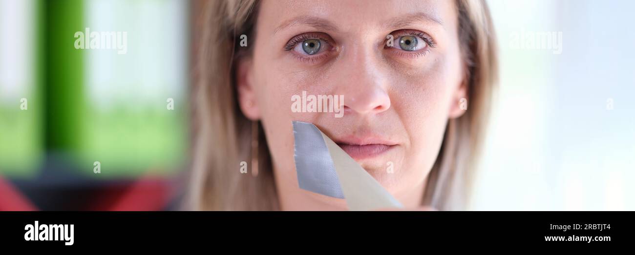 Frau entfernt Klebeband, das ihren Mund bedeckt. Stockfoto