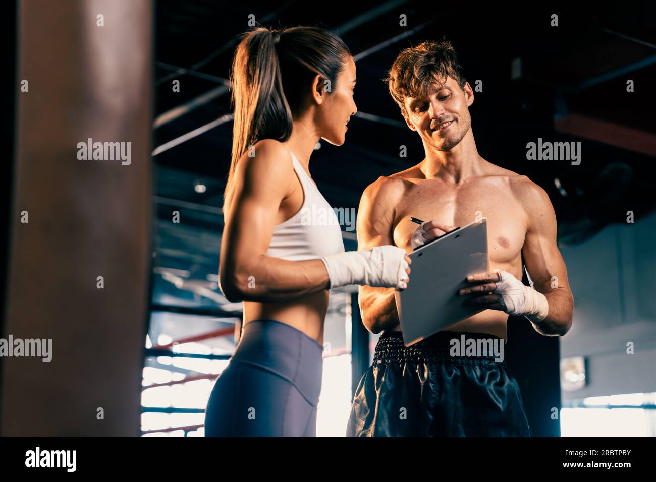Eine asiatische Muay Thai-Boxerin und ihr persönlicher Boxtrainer diskutieren über ihren körperlichen Fortschritt im Fitnessstudio, der die Bindung an ihre Körpermuskulatur widerspiegelt Stockfoto
