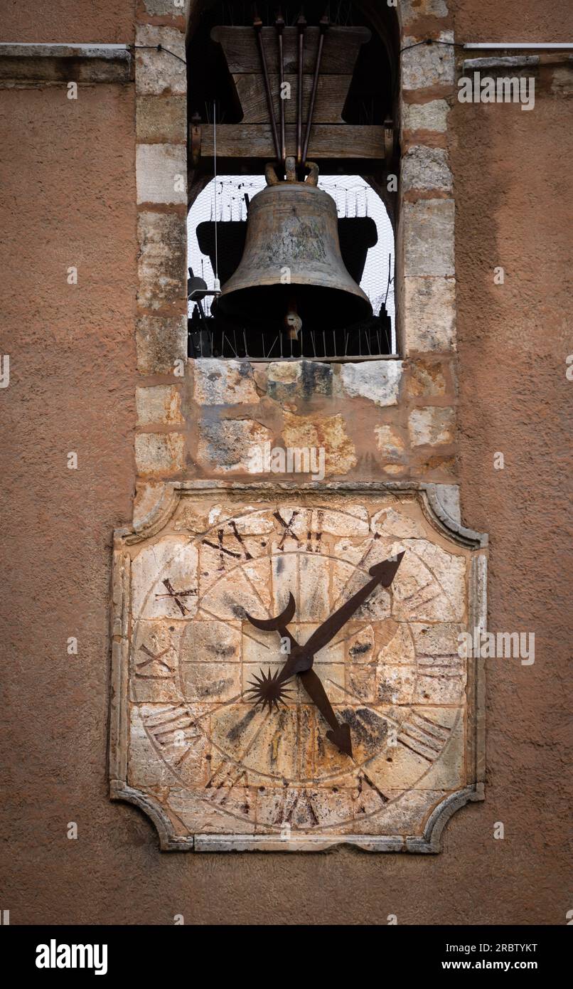 Die Steinuhr und die schmiedeeisernen Stifte einer Uhr und eine Glocke, die durch den Lauf der Zeit aus einem alten Steinturm verewigt wurde. Stockfoto