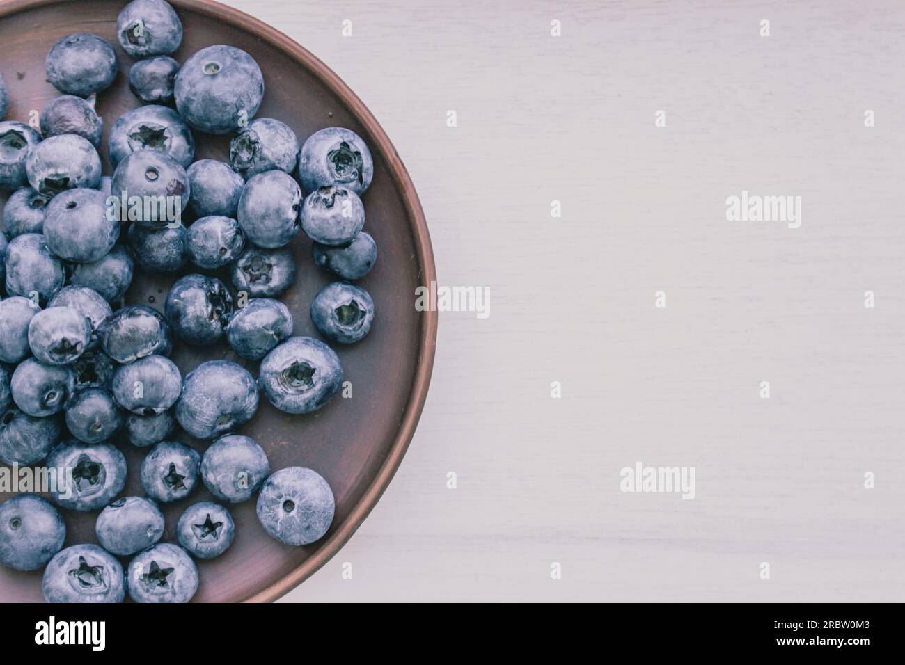 Blaubeeren auf weißem Hintergrund mit Kopierbereich. Heidelbeeren in Keramikschüssel. Antioxidative Beeren. Rohes Essen. Süße reife Beeren. Stockfoto