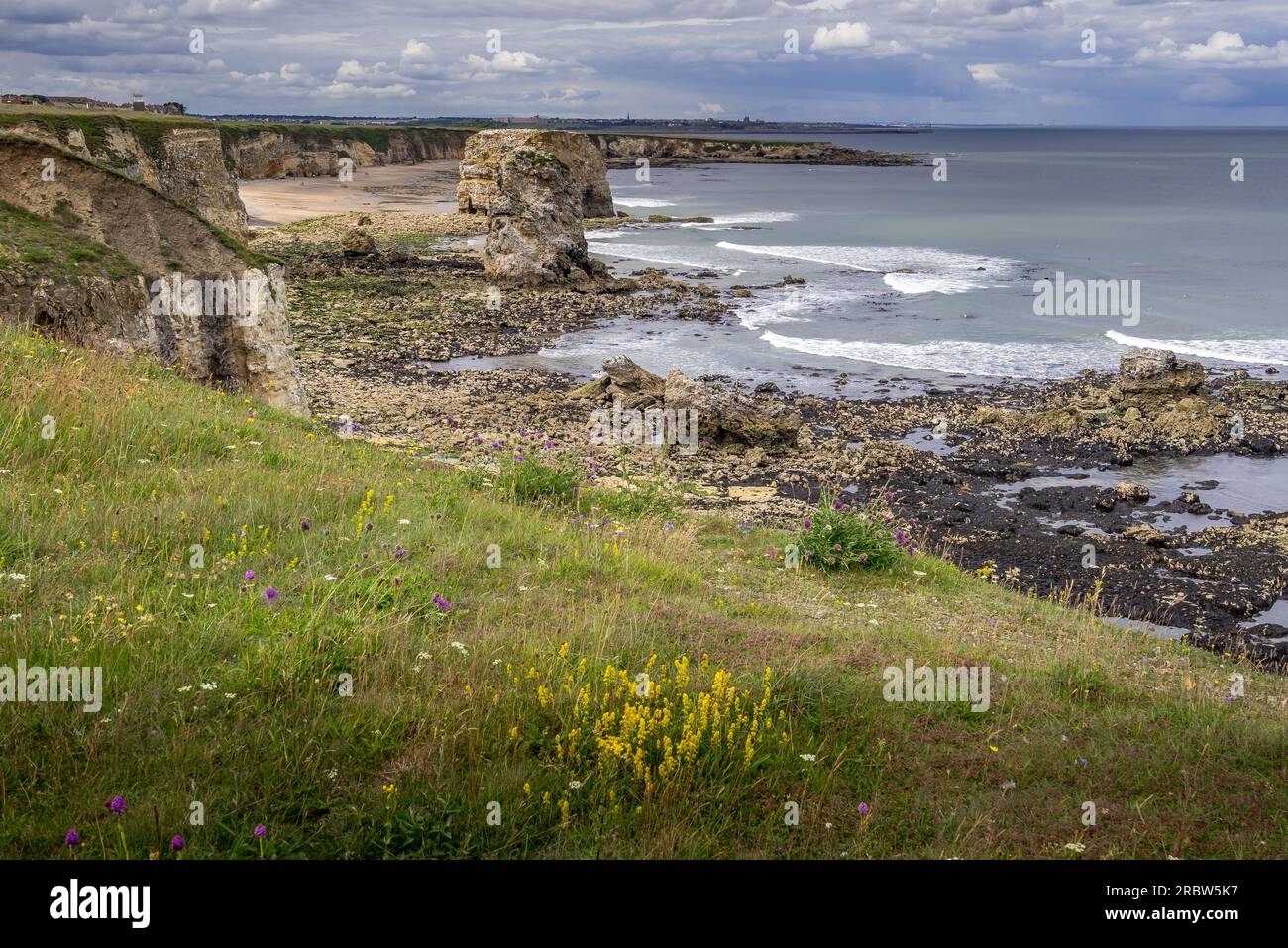 Blick von den Klippen auf Marsden Sands und Marsden Rock. In der Ferne kann man einfach die Pirs und Leuchttürme in Tynemouth erkennen Stockfoto