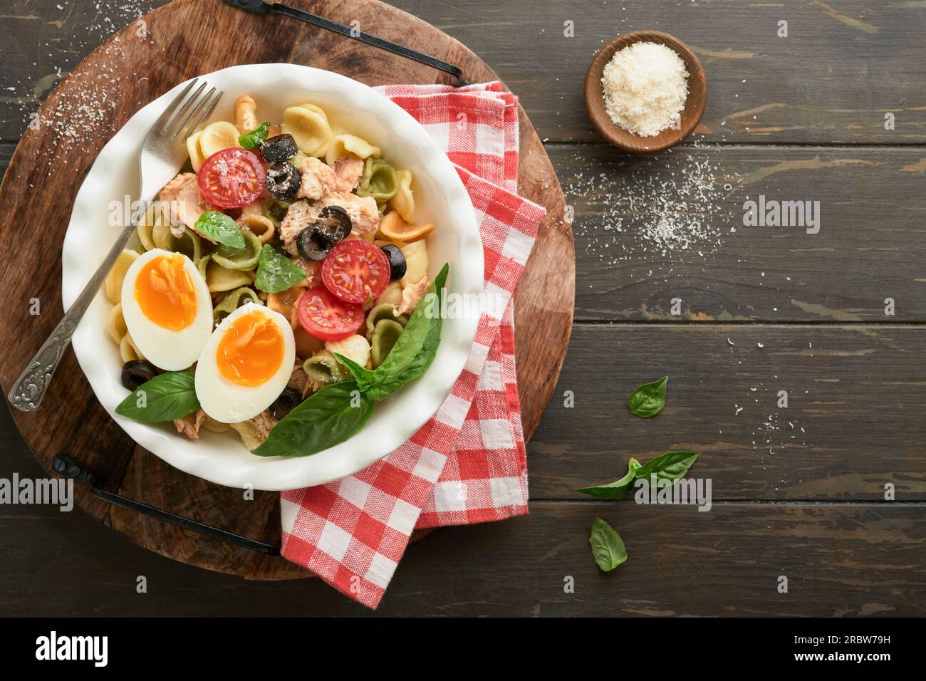 Italienischer Nudelsalat. Orekchiette Pasta mit Thunfisch, Tomatenkirsche, Oliven, Basilikum und Parmesan auf einem dunklen Holztisch mit altem rustikalem Hintergrund. Stockfoto