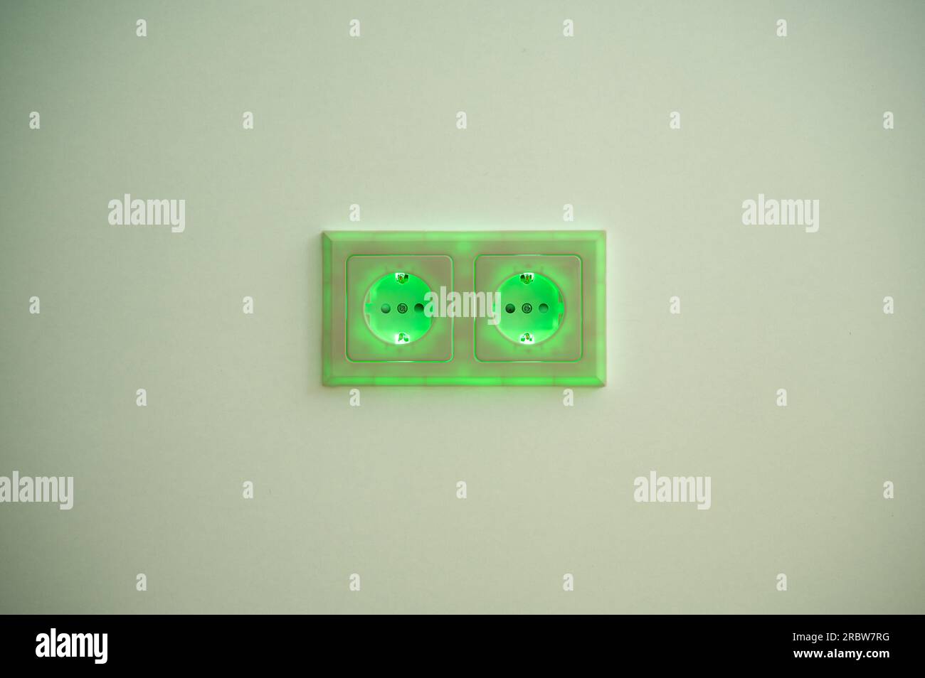 Grün beleuchtete Buchse mit eingestecktem Stecker zur Darstellung des Stromverbrauchs und der elektrischen Energie aus einer Steckdose, die umweltfreundliche und saubere Energie liefert Stockfoto