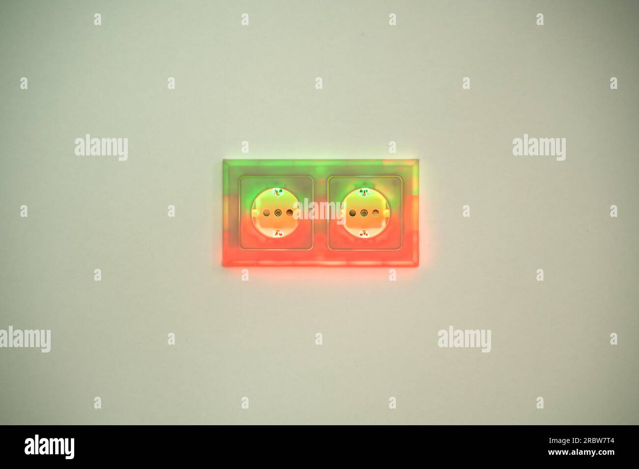 Rot und grün beleuchtete Buchsen symbolisieren den Stromverbrauch und die elektrische Energie aus der Steckdose, die während der Energiewende grüne Energie liefert Stockfoto