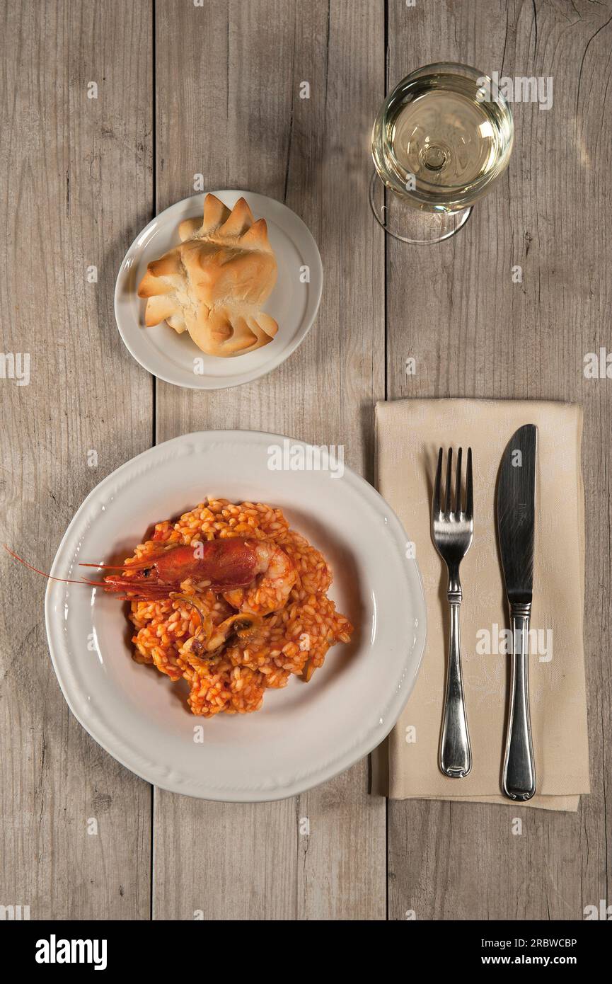 Risotto mit roten Garnelen, Tintenfisch, Fischfilets, Tomaten. Brot und Weißwein. Nach dem Kochen Stockfoto
