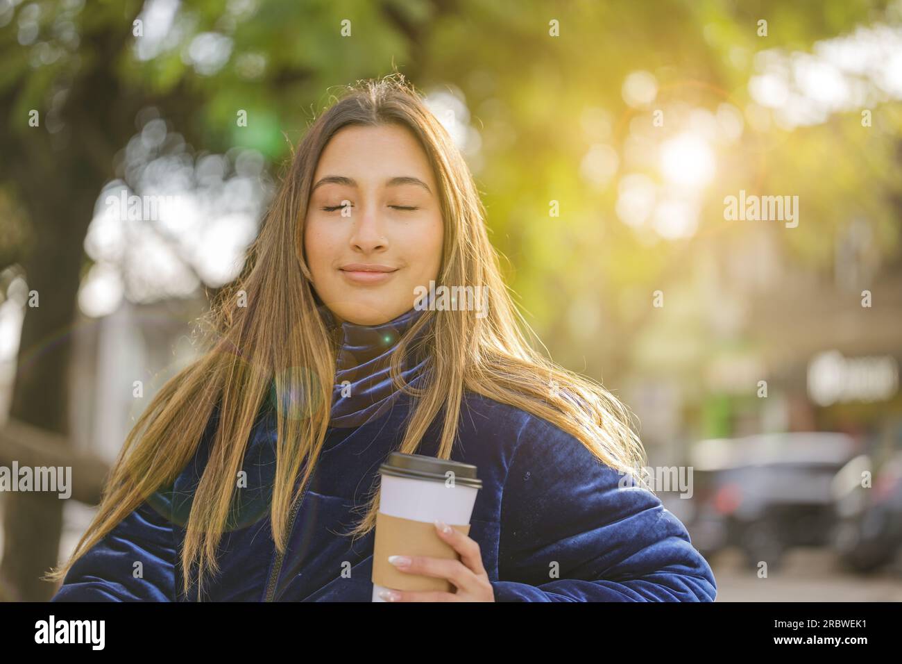 Ein lateinisches Mädchen mit geschlossenen Augen genießt ihren Kaffee in einem öffentlichen Park. Stockfoto