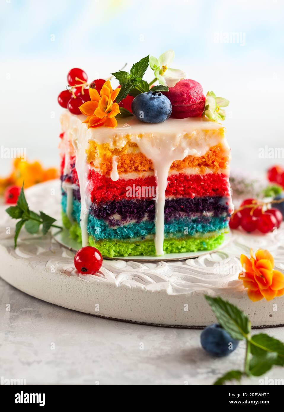 Ein Stück Regenbogenkuchen mit frischen Beeren und Blumen für den Urlaub Stockfoto