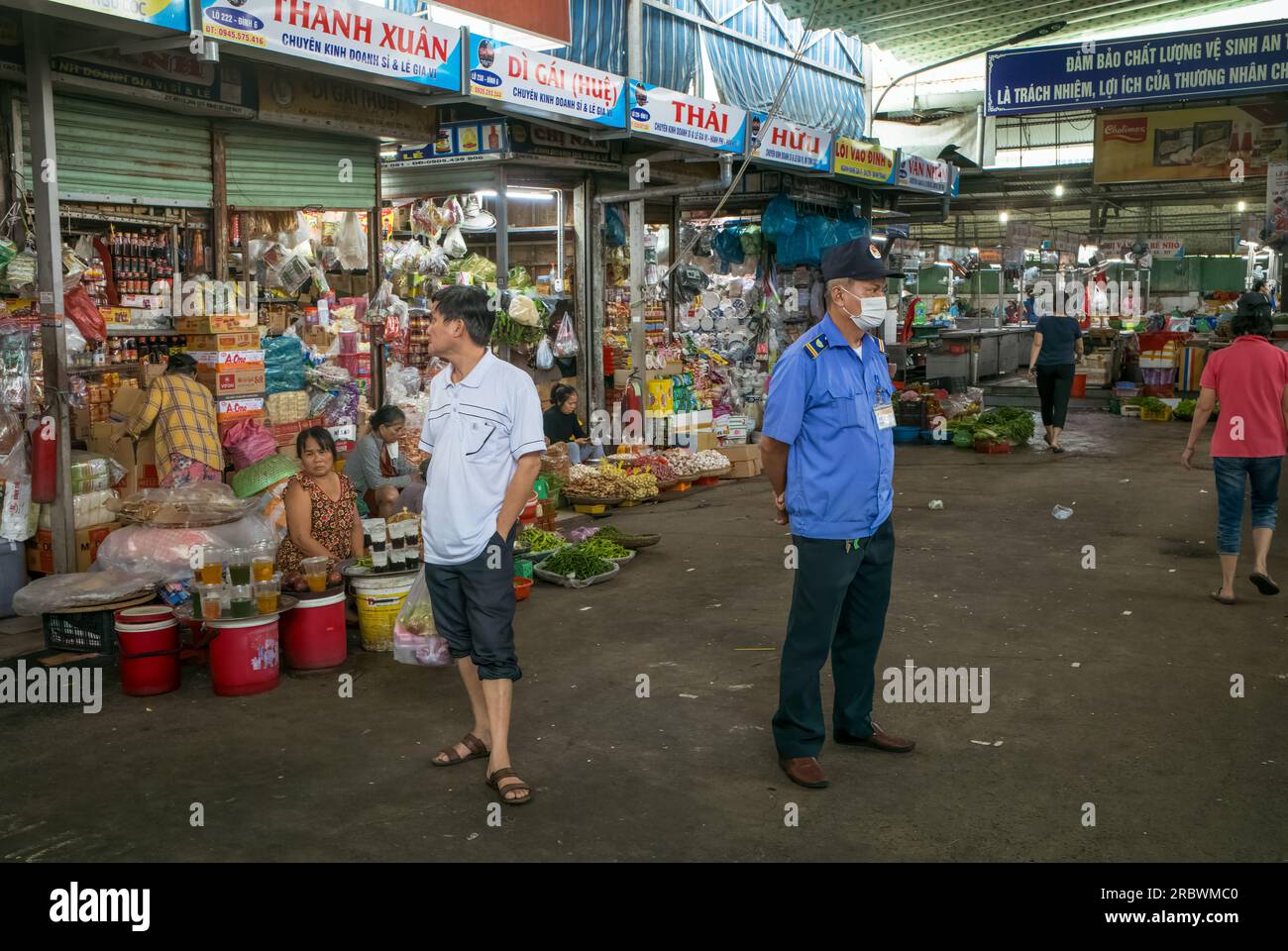 Ein uniformierter Wachmann und ein Käufer stehen einander gegenüber neben Verkaufsständen in Con Market, Danang, Vietnam. Stockfoto