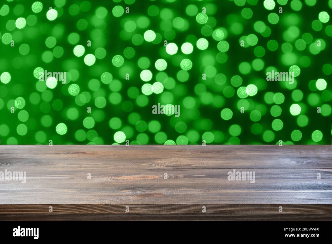 Unscharfe grüne Girlande und leere Tischplatte aus Holz als Hintergrund für Design. Festliches abstraktes Muster. Stockfoto