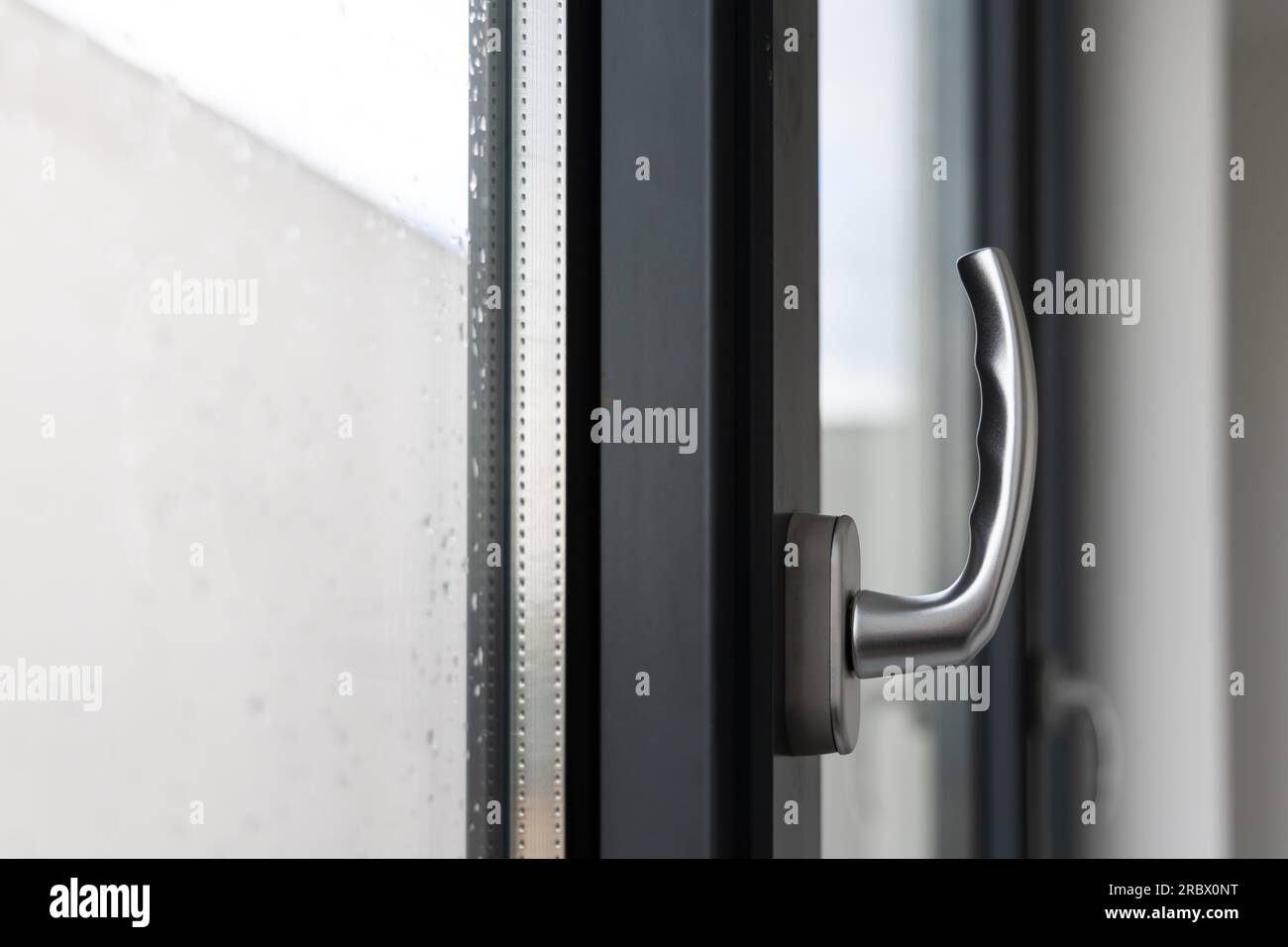 Neigen und Drehen des Fenstergriffs in einem großen Fenster in einem öffentlichen Gebäude. Das Fenster besteht aus sichtbaren Silikondichtungen aus Kunststoff. Stockfoto