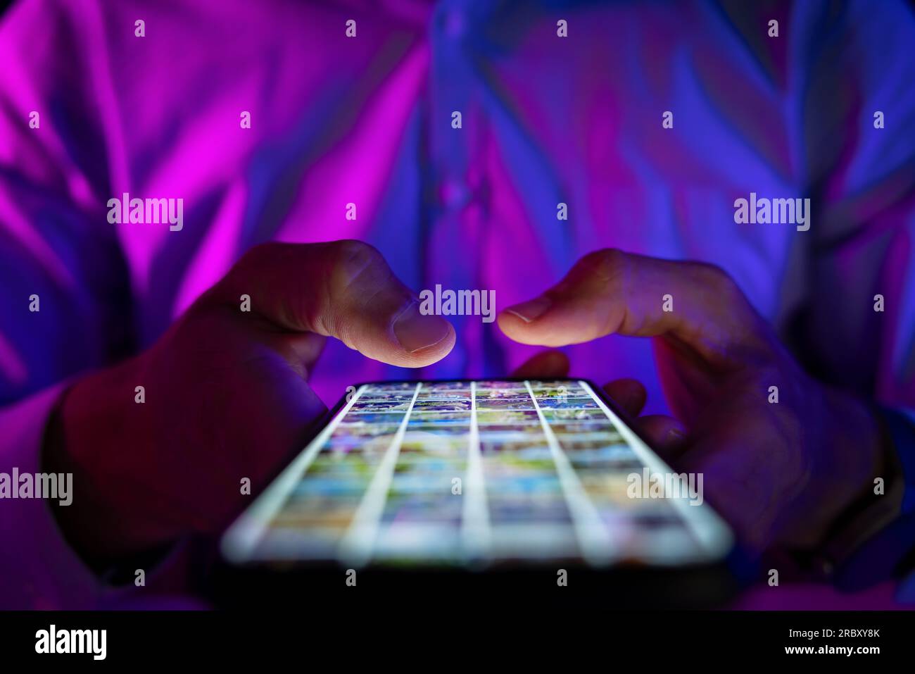 Mann, der in einem dunklen Raum mit Neonlichtern auf dem Handy scrollt. surfen im internet, soziale Medien und Marketing Stockfoto