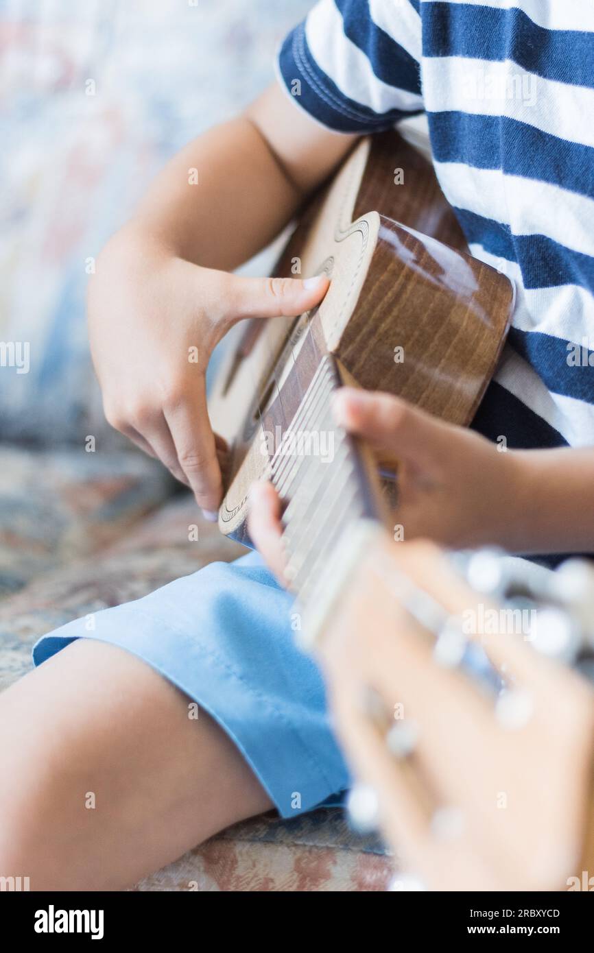 Kaukasisches Kind spielt und macht Musikakkorde mit kleiner Gitarre oder Ukulele, Nahaufnahme Stockfoto