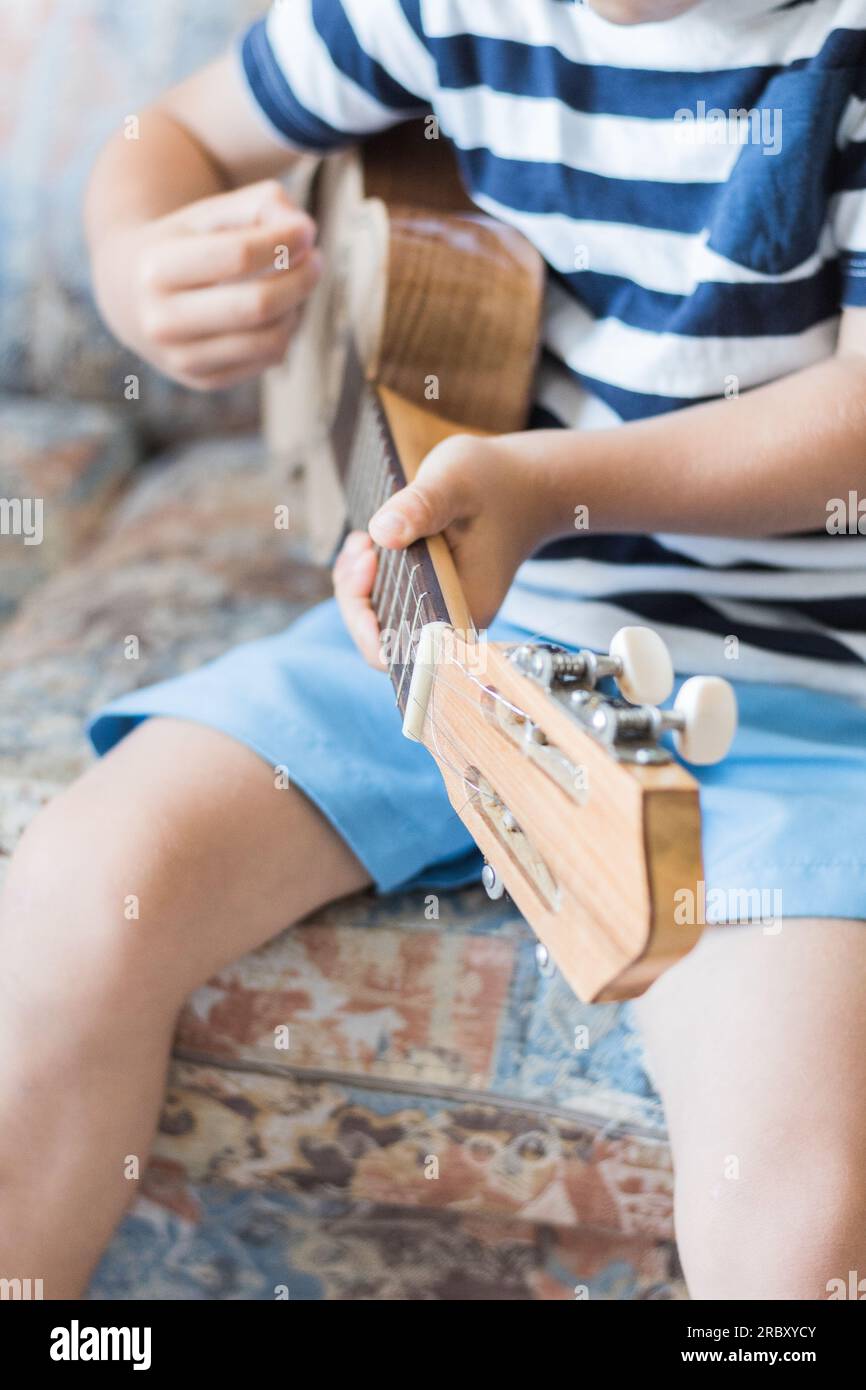 Kaukasisches Kind spielt und macht Musikakkorde mit kleiner Gitarre oder Ukulele, Nahaufnahme Stockfoto