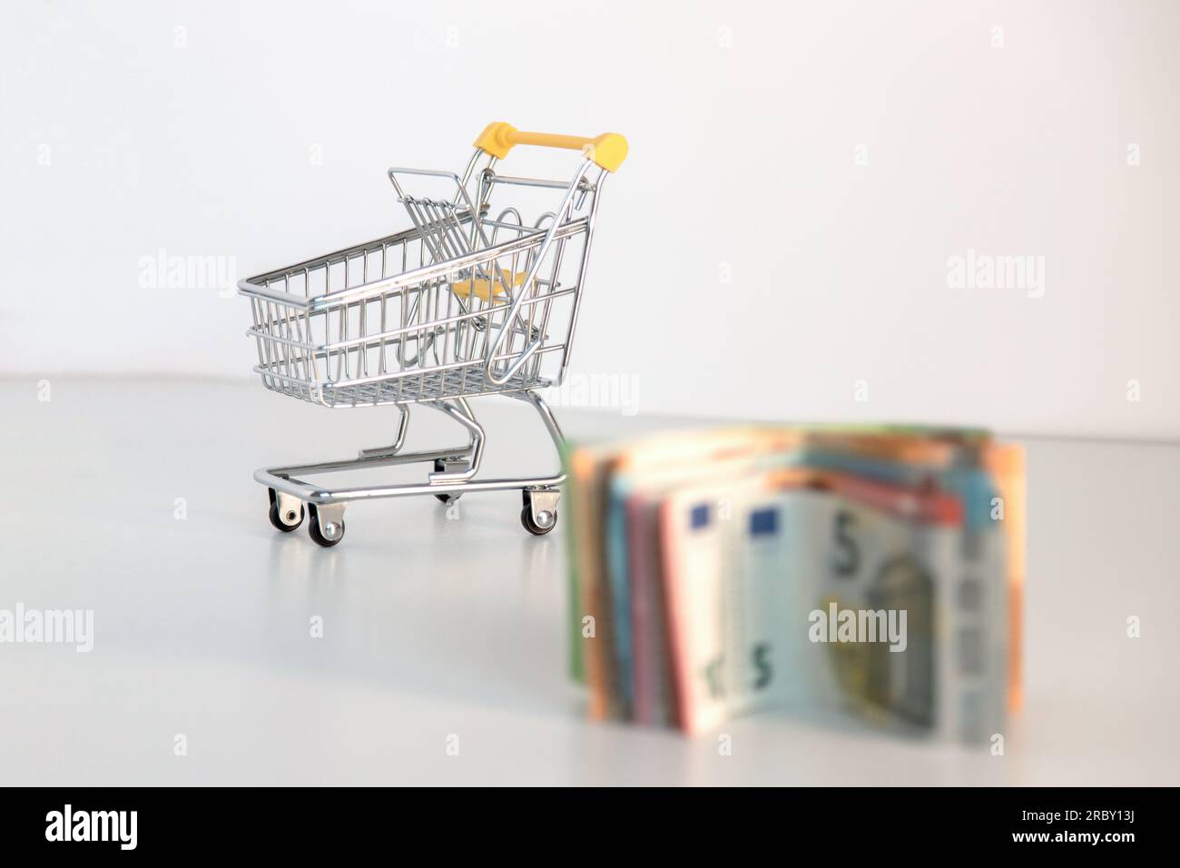 Supermarkt-Einkaufswagen mit wichtigen Waren und mehreren Euro-Banknoten auf weißem Hintergrund. Konzeptionelles Bild der Kaufkraft. Stockfoto