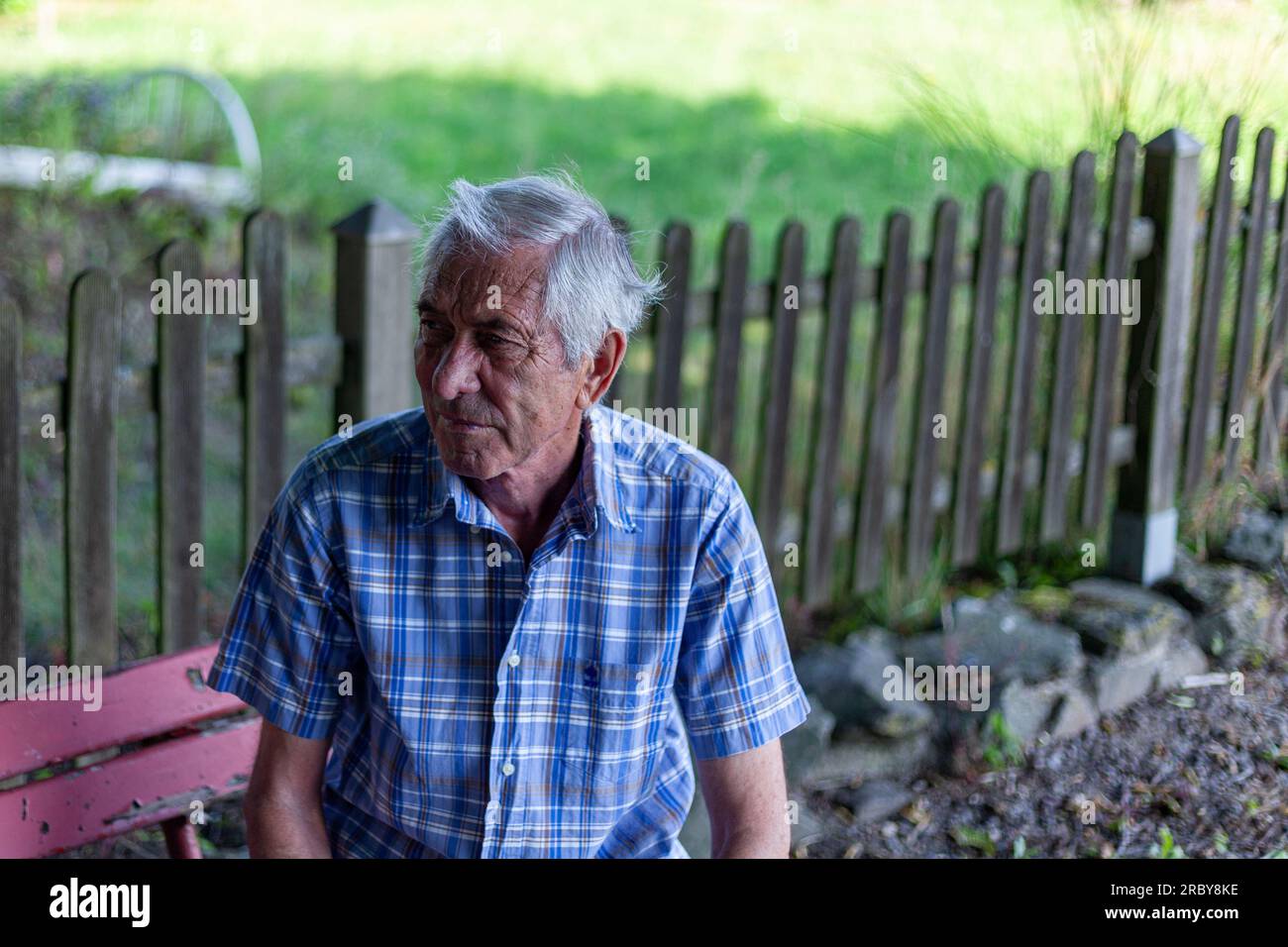 Älterer Mann, der auf einer Bank im Garten sitzt und in die Kamera schaut Stockfoto
