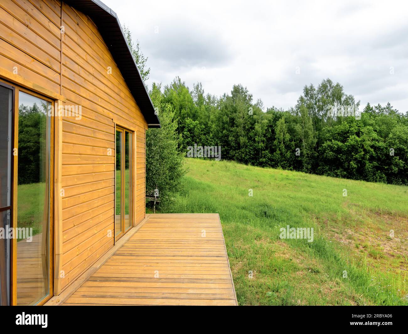 Hölzernes Bauernhaus in der Natur, grünes Gras und Wald, Himmel. Stockfoto