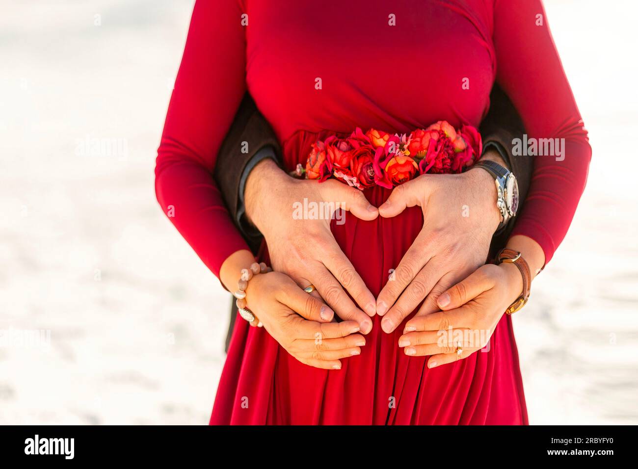 Schwangere Frau und ihr Mann umarmen sich und machen Herzen mit ihren Händen Stockfoto