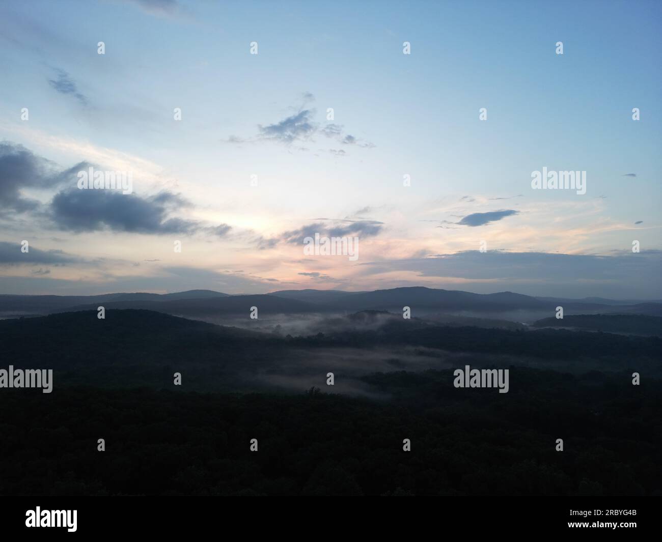 Drohnenbild eines nebeligen Tals mit sanften Hügeln bei Sonnenuntergang Stockfoto
