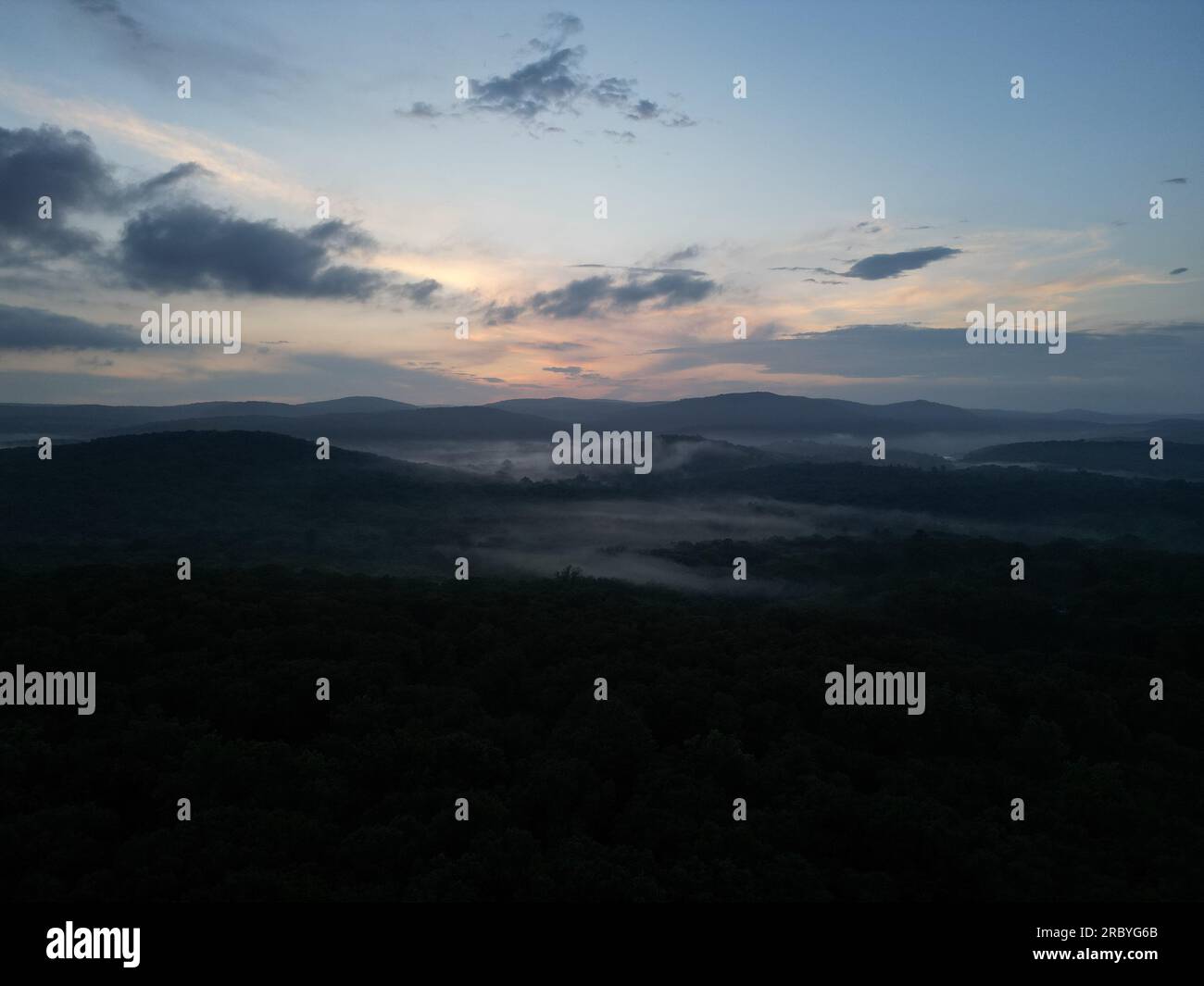 Drohnenbild eines nebeligen Tals mit sanften Hügeln bei Sonnenuntergang Stockfoto