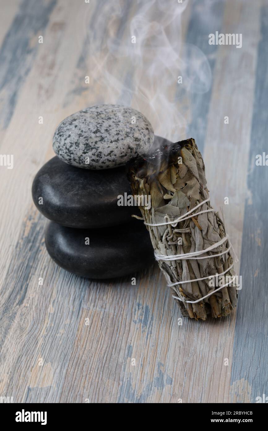 Ein leuchtender weißer Salbeifleck klebt neben den Steinen. Für Meditation, Heilung und spirituelle Zimmerreinigung. Stockfoto