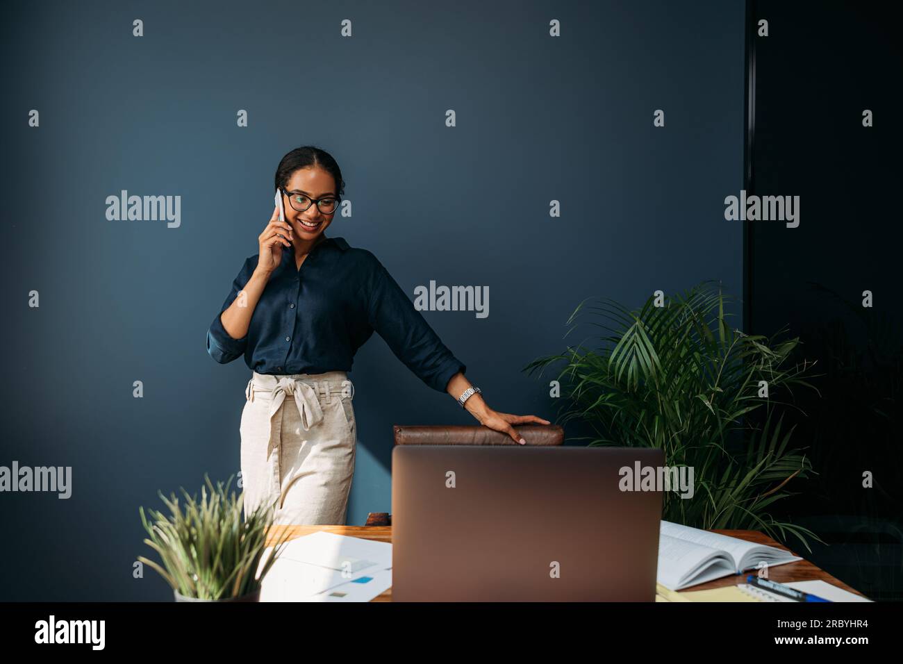 Lächelnde Geschäftsfrau, die telefoniert, während sie im Wohnzimmer am Schreibtisch steht Stockfoto