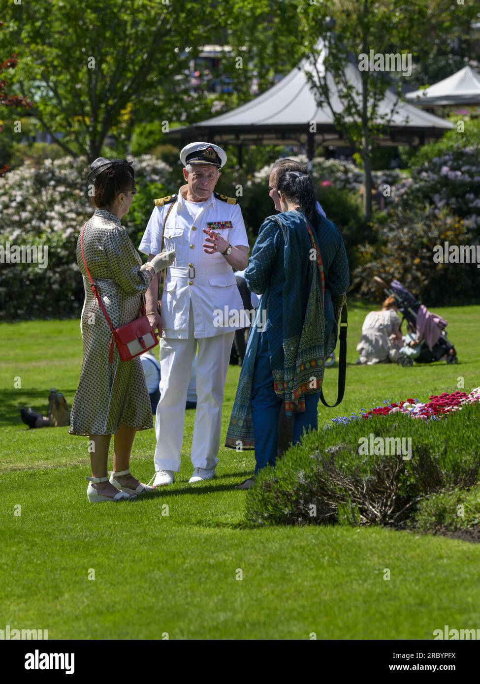 Eine Person in der Mode der 1940er Jahre (Offizierskostüm) bei einem nostalgischen Nachstellungswochenende, die sich mit dem sonnigen Haworth Park, West Yorkshire England, unterhalten hat. Stockfoto