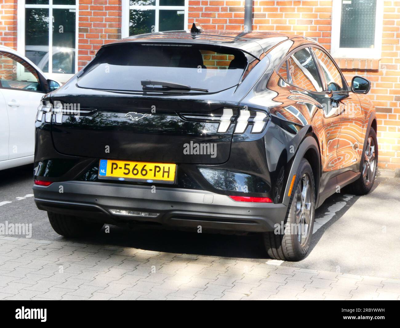 Uelsen, Deutschland - Juni 27 2023 Ein schwarzer Ford Mustang Mach-E parkt vor einer Mauer. Die Wand spiegelt sich im Auto wider. Dieser Mustang ist elektrisch Stockfoto