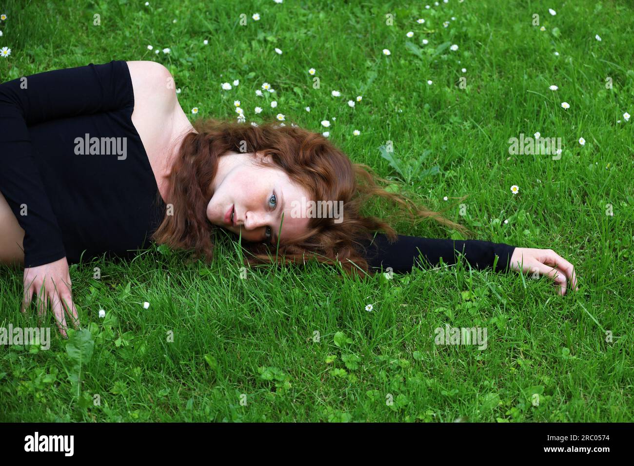 Porträt eines sinnlichen Ingwermädchens mit langen roten Haaren und Sommersprossen, das im Sommerpark auf dem Gras liegt Stockfoto