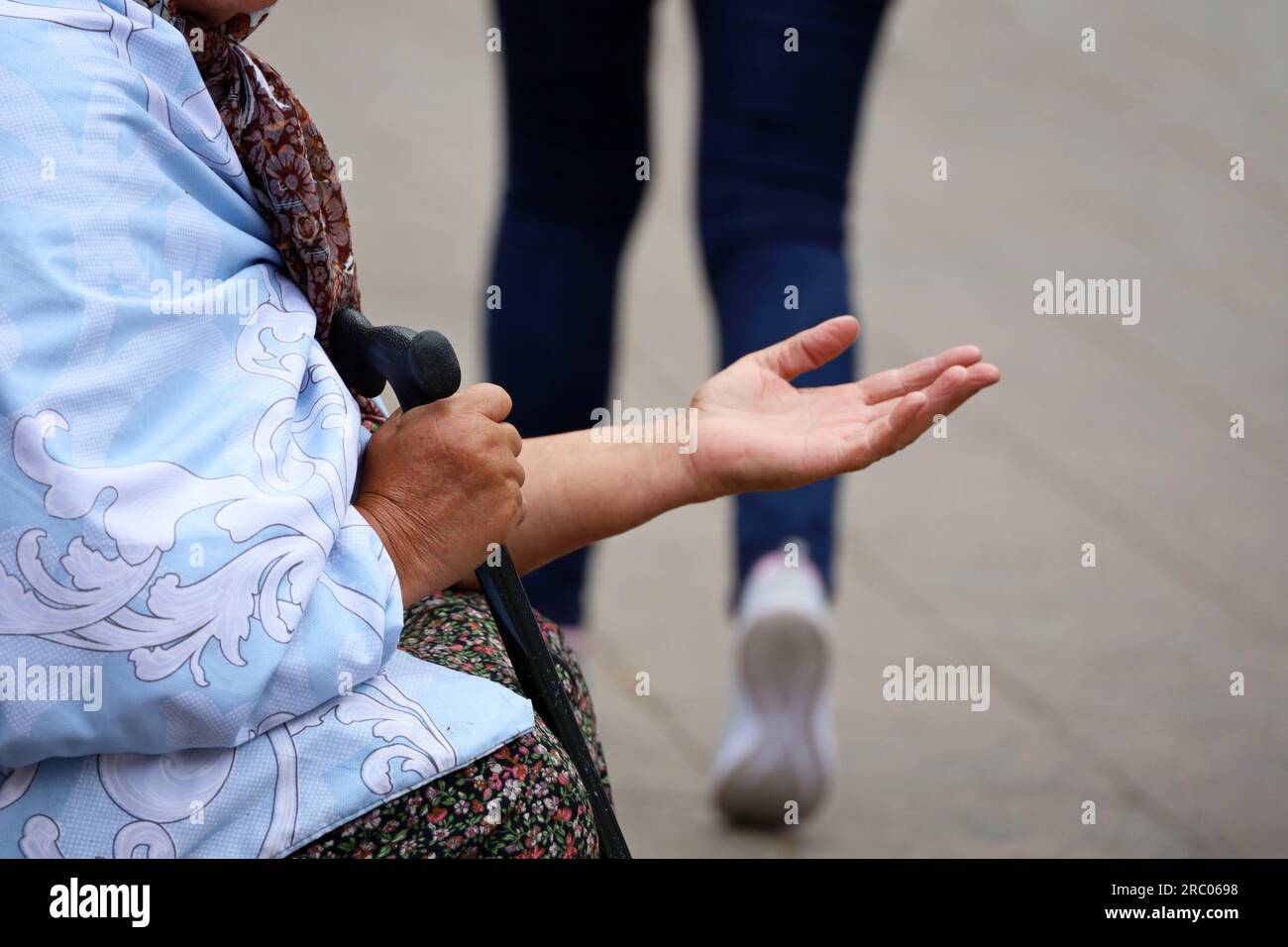 Die alte Bettler bittet um Almosen, die auf einer Straße mit ausgestreckter Hand sitzen. Armut, Obdachlosigkeit und Bettelei Stockfoto