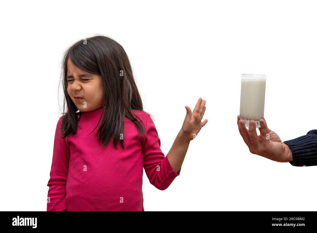 Das Mädchen der Grundschule lehnt ein Glas Milch ab, das ihr auf weißem Hintergrund angeboten wird Stockfoto
