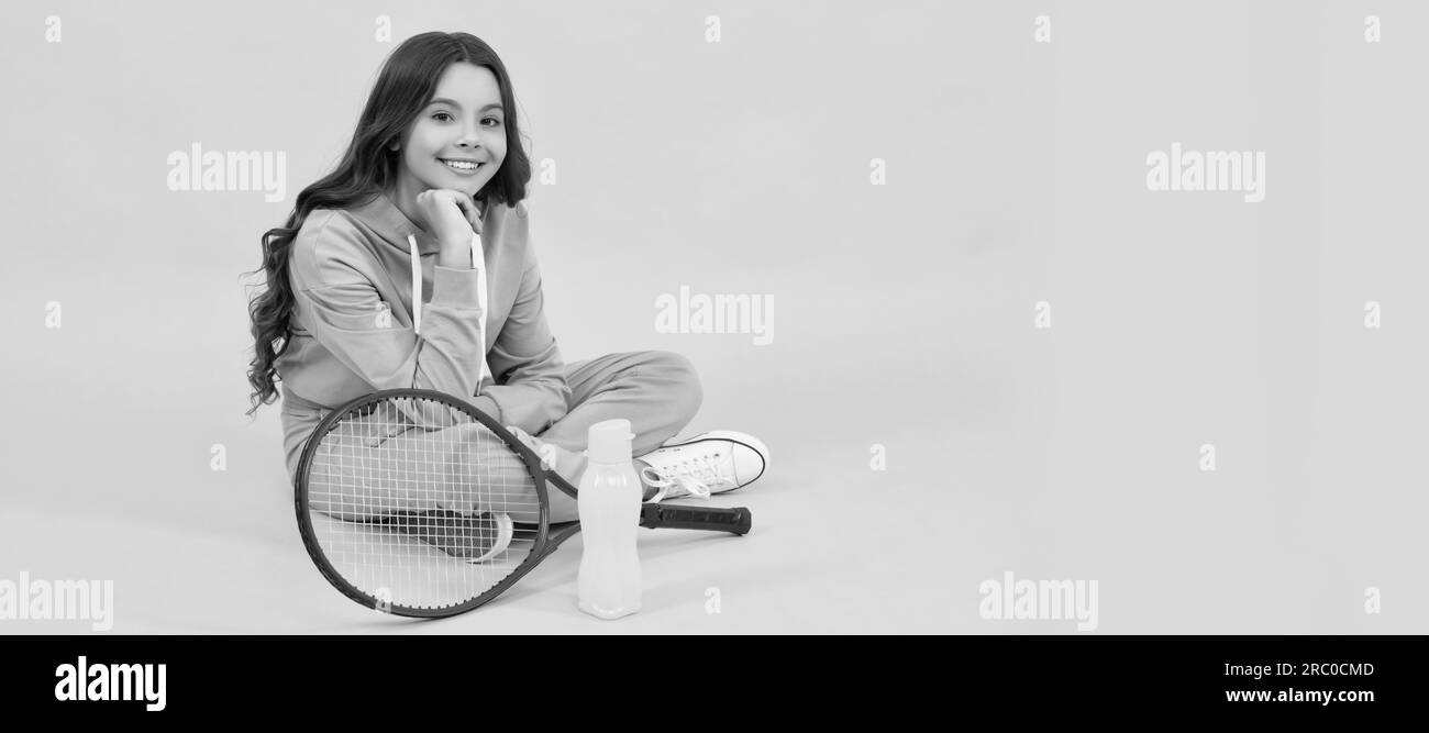 Fröhliches Kind sitzt in Sportkleidung mit Badminton-Schläger und Wasserflasche auf gelbem Hintergrund, entspannen. Horizontales Poster mit isoliertem Kindergesicht, Banner Stockfoto