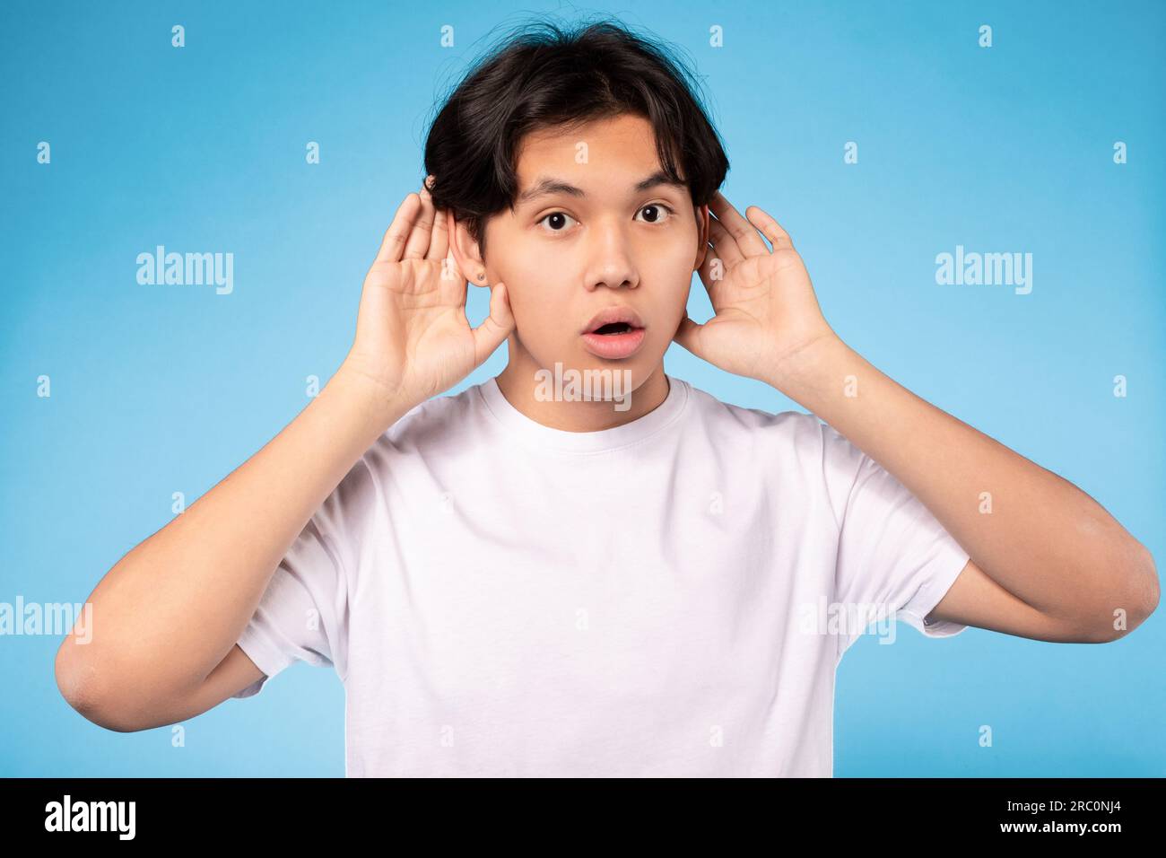 Asiatischer Teenager, Der Zuhört, Hände An Ohren Hält, Blauer Hintergrund Stockfoto