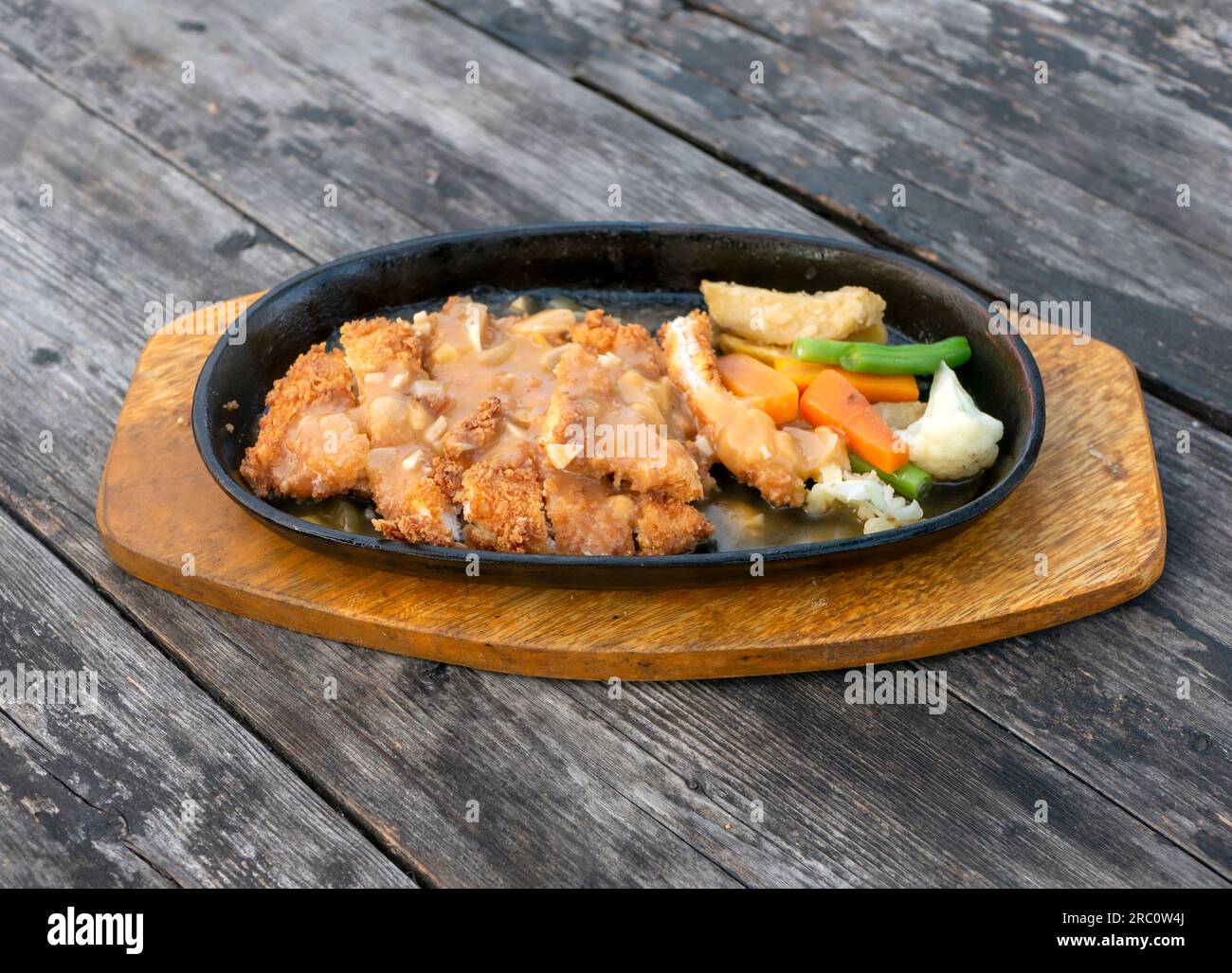 Gebratenes Hähnchen auf der Warmhalteplatte, mit Gemüse, auf einem alten alten Holztisch Stockfoto