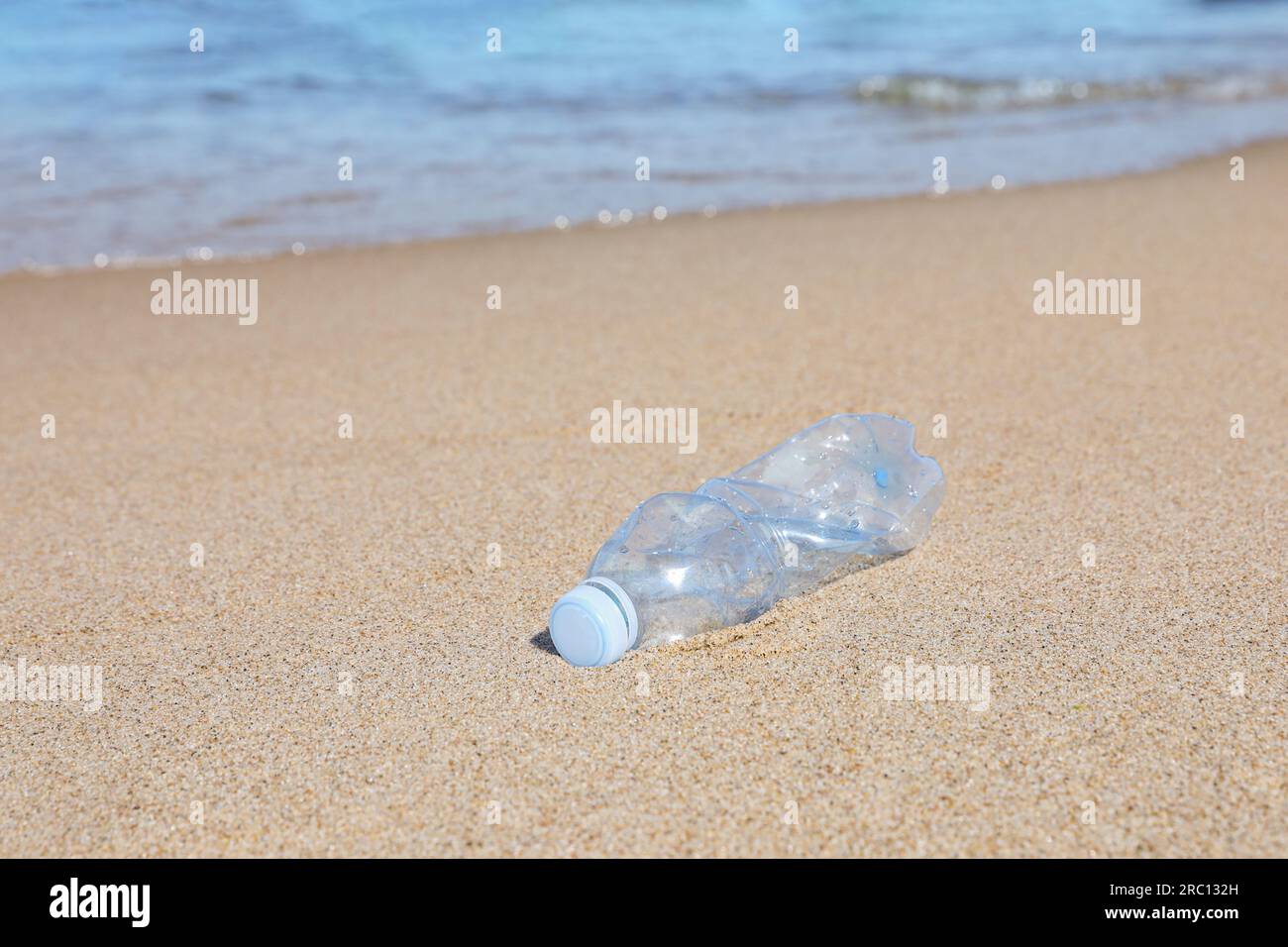 Benutzte Plastikflasche auf Sand in der Nähe von Wasser. Recycling-Problem Stockfoto