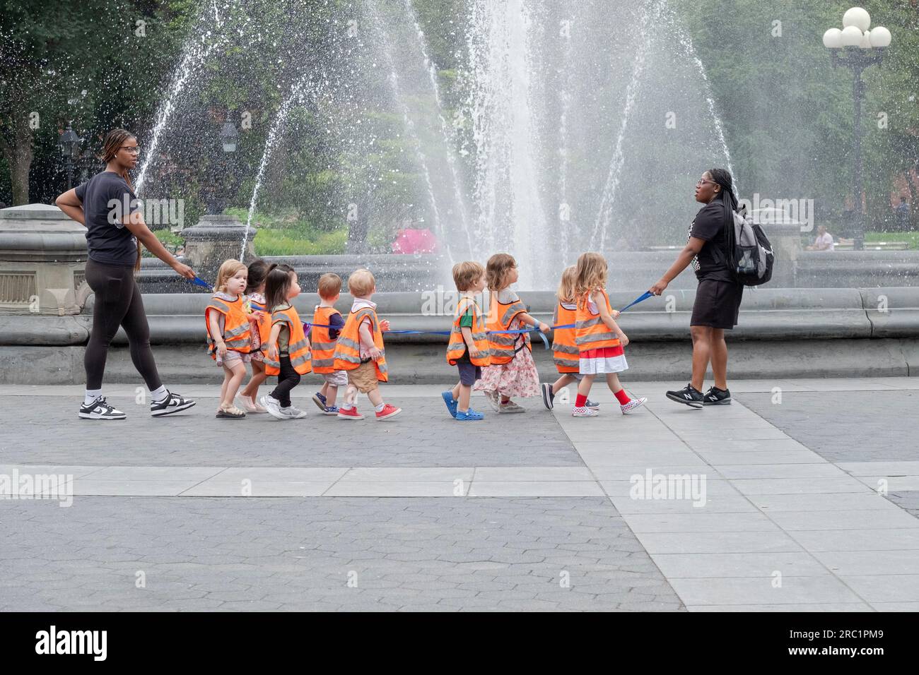 Eine Tagesbetreuung in orangefarbenen Westen am Brunnen im Washington Square Park in Manhattan, New York City. Stockfoto