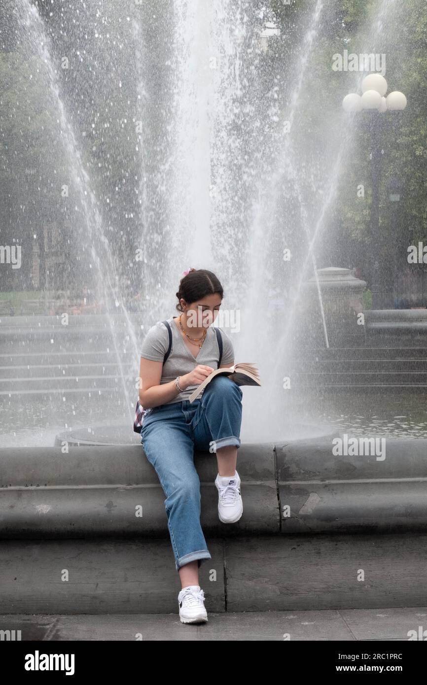 Eine junge Dame, wahrscheinlich eine Studentin, liest ein Buch in der Nähe des Brunnens im Washington Square Park in Greenwich Village, Manhattan, New York City. Stockfoto