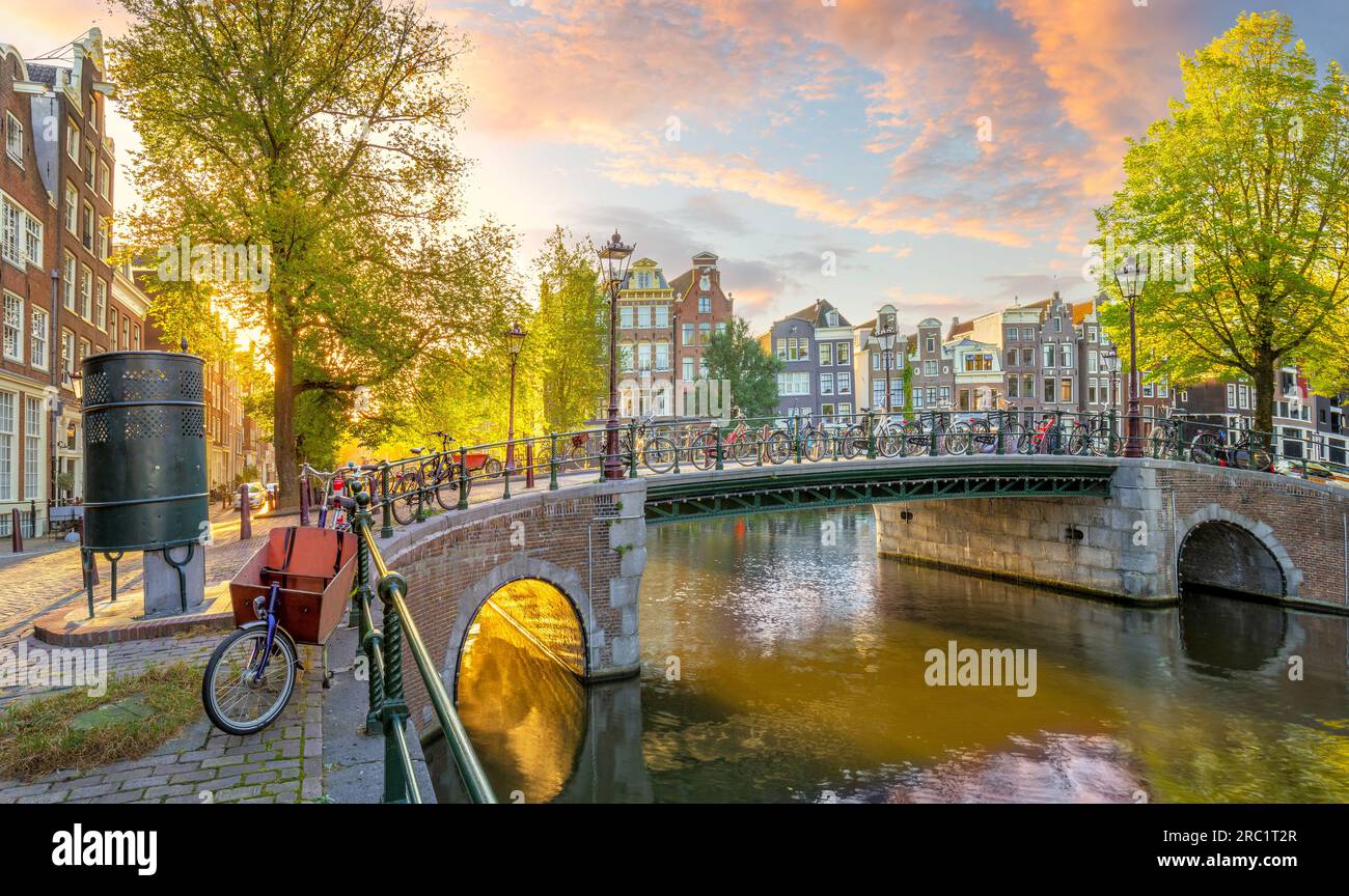 Die Seele von Amsterdam. Am frühen Morgen in Amsterdam. Alte Häuser, Brücken, traditionelle Fahrräder, Kanäle und die Sonne scheint durch die Bäume. Panorama V Stockfoto