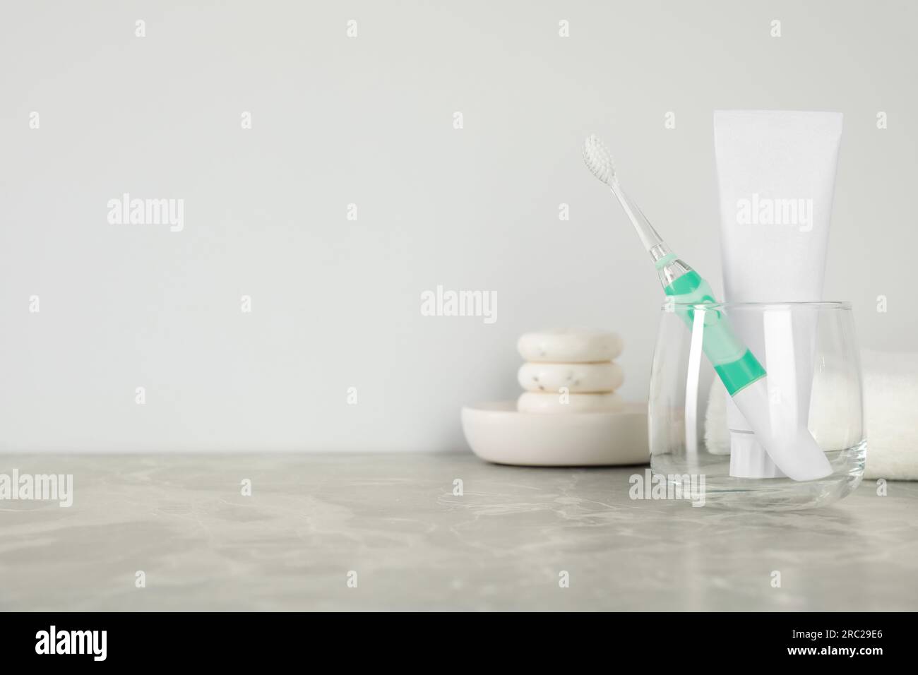 Elektrische Zahnbürste aus Glas und Tube mit Paste auf hellgrauem Marmortisch. Platz für Text Stockfoto