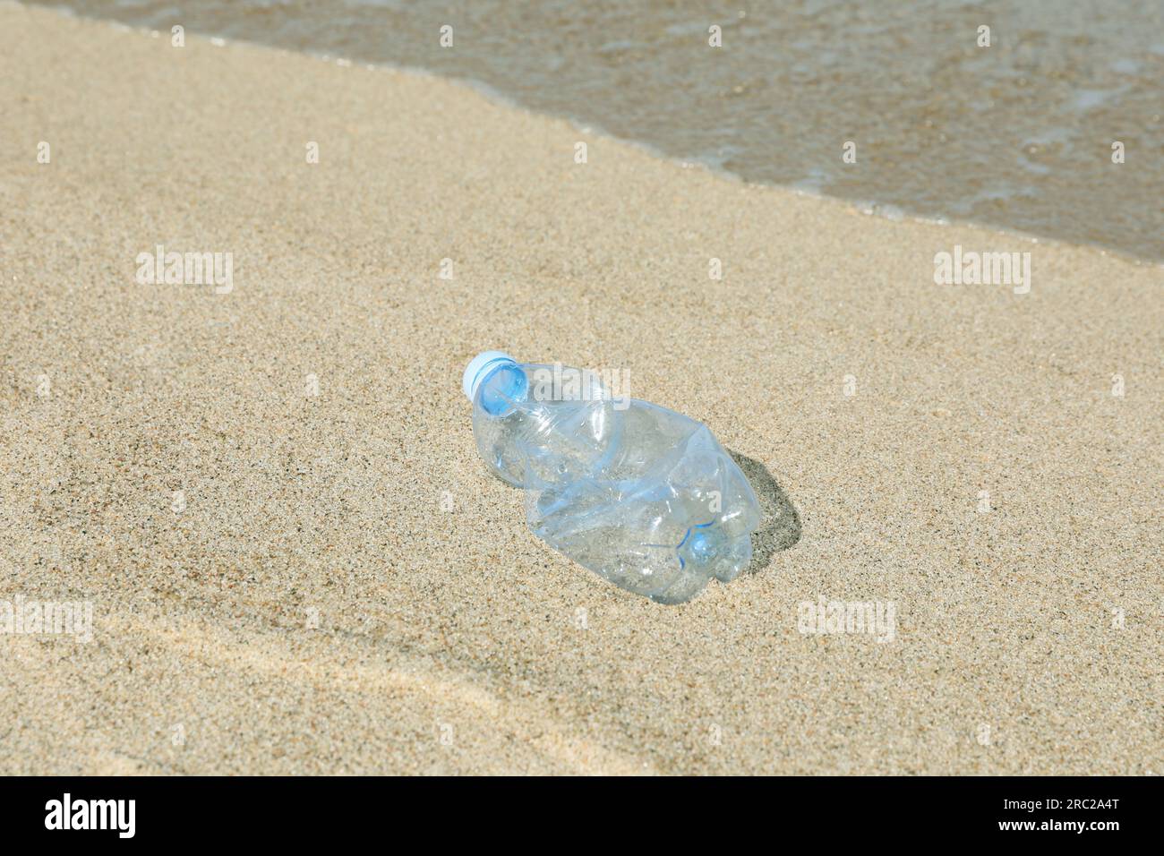 Benutzte Plastikflasche auf Sand in der Nähe von Wasser. Recycling-Problem Stockfoto