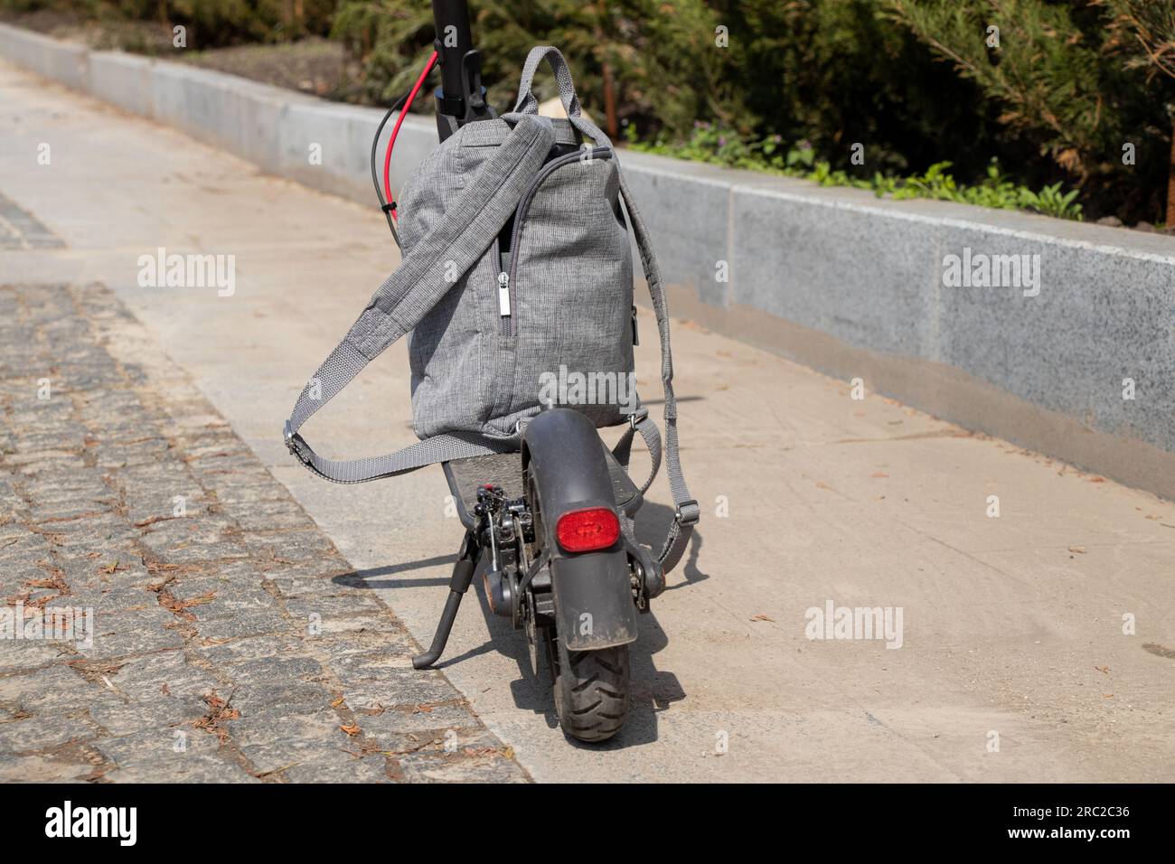 Ein grauer urbaner Rucksack steht auf einem elektrischen Roller im Sommer auf der Straße in der Sonne in der Stadt, im Lifestyle, im Stadtverkehr und in der Mode Stockfoto