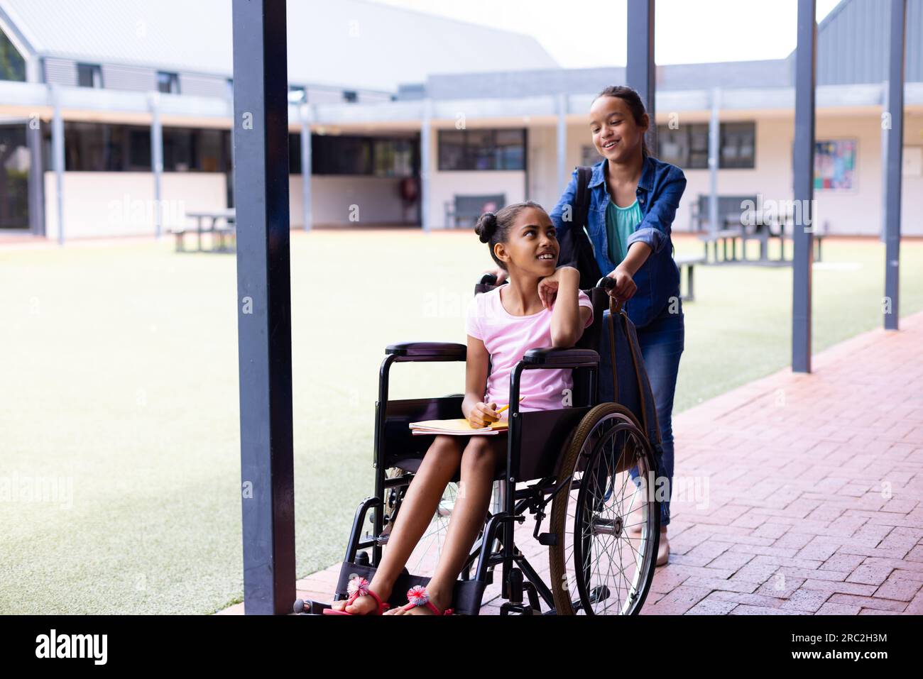 Fröhliches, vielseitiges Schulmädchen im Rollstuhl mit ihrer Freundin in der Schule Stockfoto