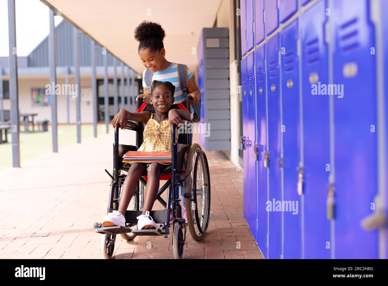 Glückliches afroamerikanisches Schulmädchen im Rollstuhl mit ihrer Freundin im Schulhof Stockfoto