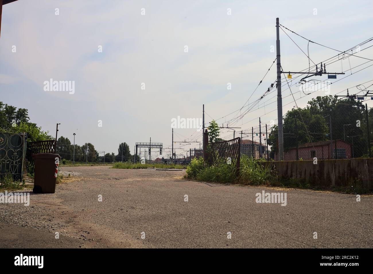 Gepflasterte Straße neben Bahngleisen und ein Bahnhof in der Ferne an einem sonnigen Tag in einer italienischen Stadt Stockfoto