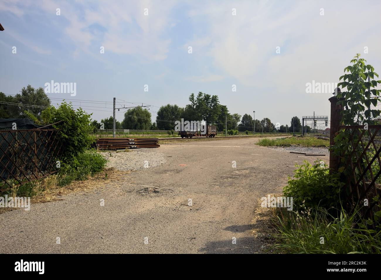Gepflasterte Straße neben Bahngleisen und ein Bahnhof in der Ferne an einem sonnigen Tag in einer italienischen Stadt Stockfoto