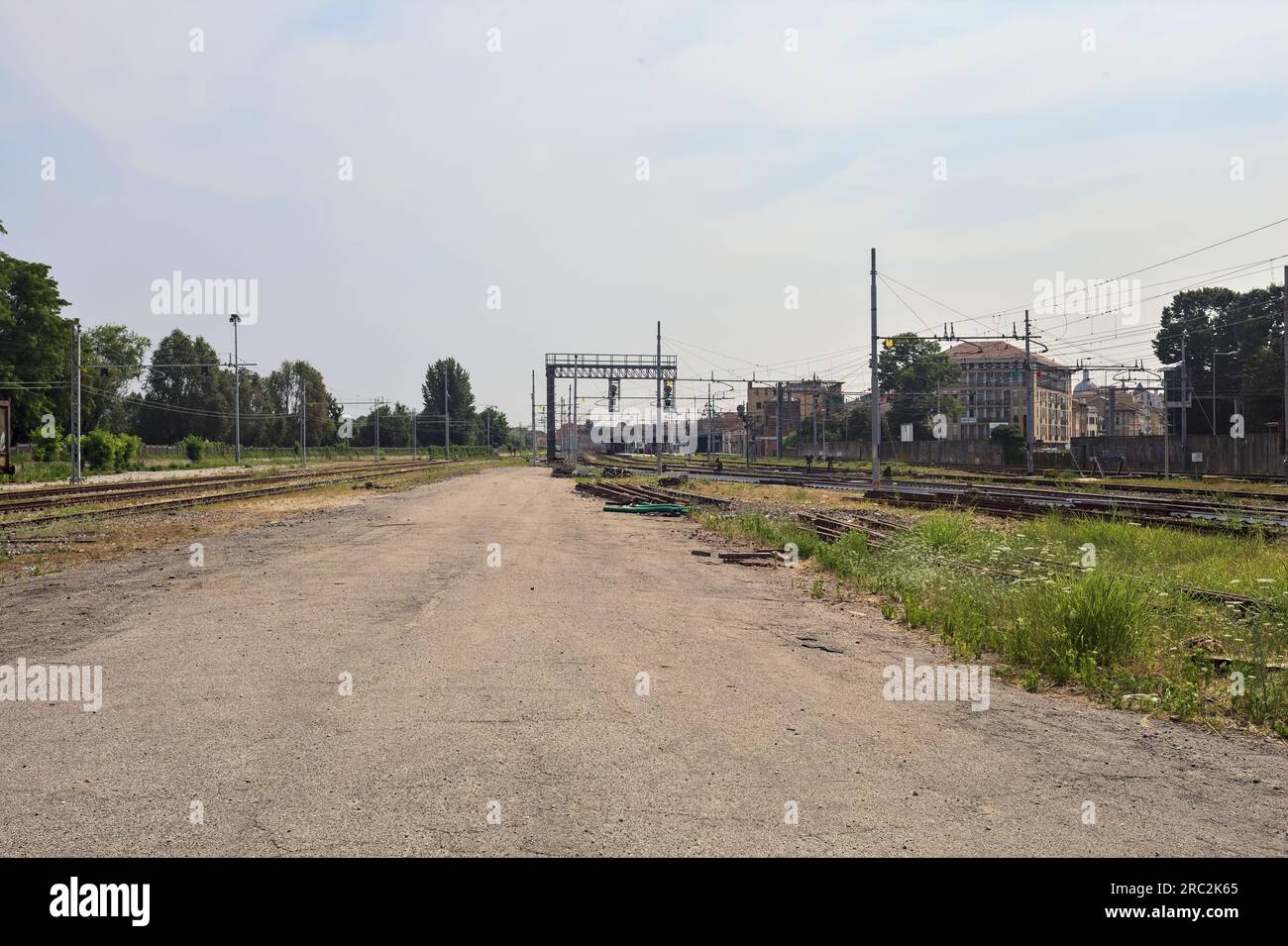 Gepflasterte Straße neben Bahngleisen und ein Bahnhof in der Ferne an einem sonnigen Tag in einer italienischen Stadt Stockfoto