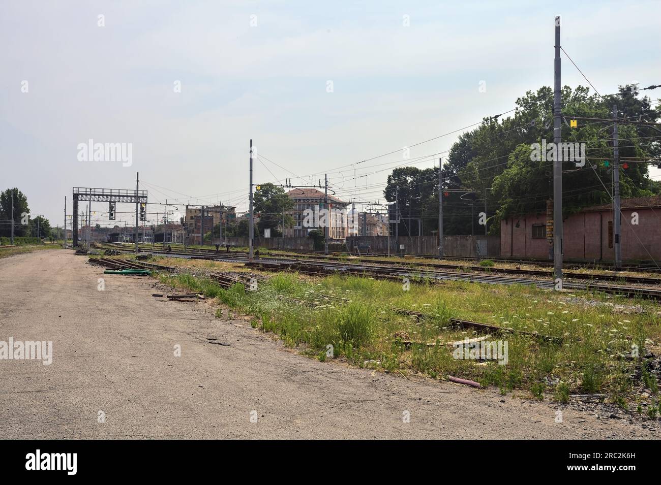 Gepflasterte Straße neben Bahngleisen und ein Bahnhof in der Ferne an einem sonnigen Tag in einer italienischen Stadt Stockfoto