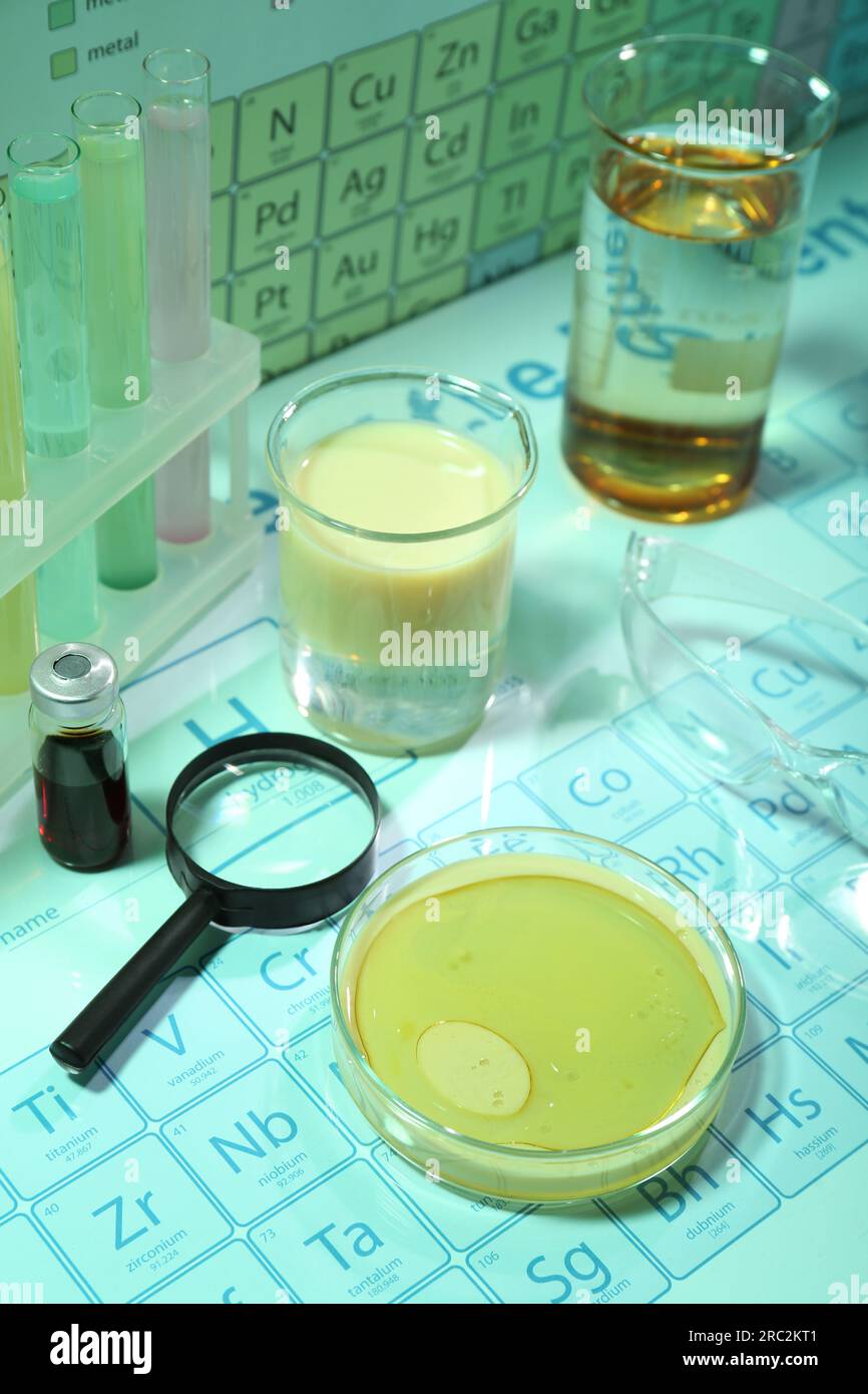 Verschiedene Laborgeräte mit Flüssigkeiten und Schutzbrillen auf dem Periodensystem chemischer Elemente. Hellgrüner Toneffekt Stockfoto