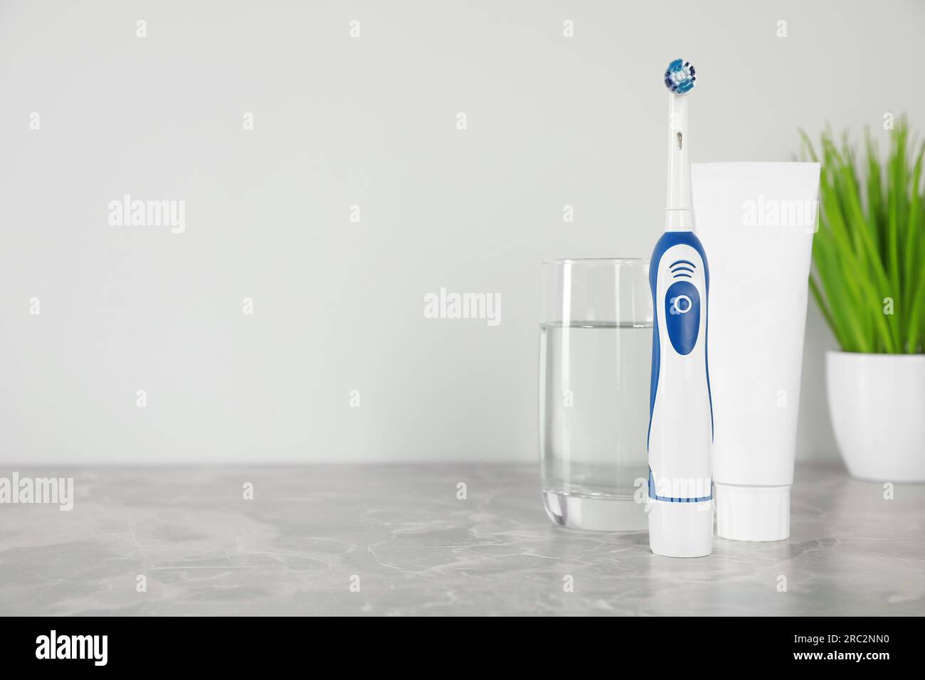 Elektrische Zahnbürste, Tube mit Paste und Glas Wasser auf hellgrauem Marmortisch. Platz für Text Stockfoto